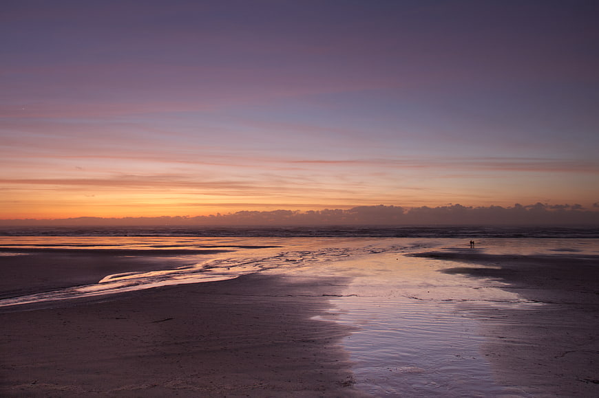 Serene Sunset Seascape with Wet Sand Reflections and Distant Figures