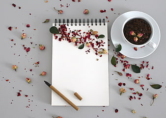 Flat lay of notebook, pen, and coffee cup with dried rose petals