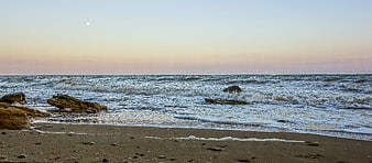 Panoramic sunset beach with waves, rocks, and moon