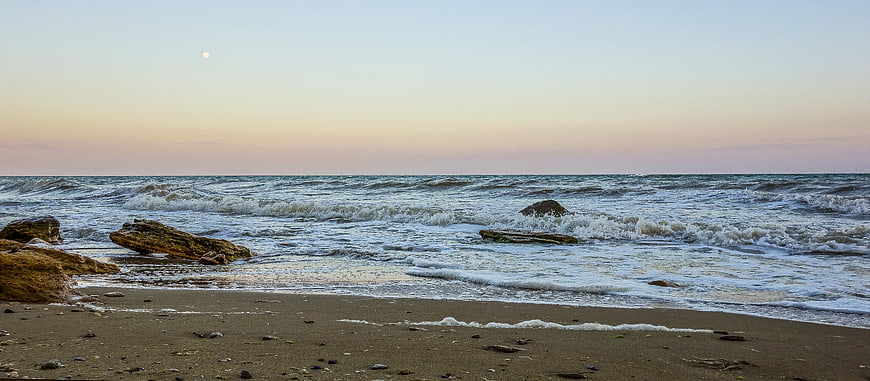 Panoramic sunset beach with waves, rocks, and moon