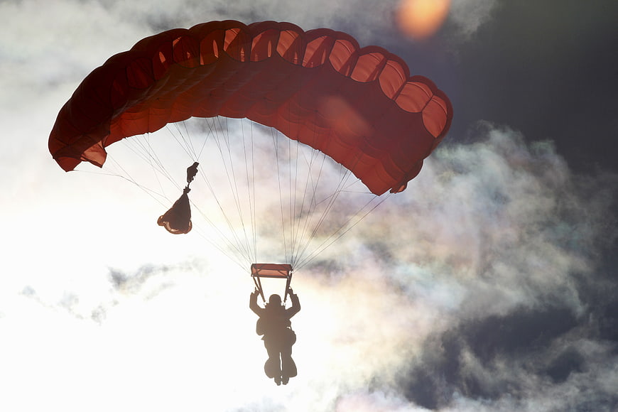 Silhouette of Paratrooper with Red Parachute Against Cloudy Sky