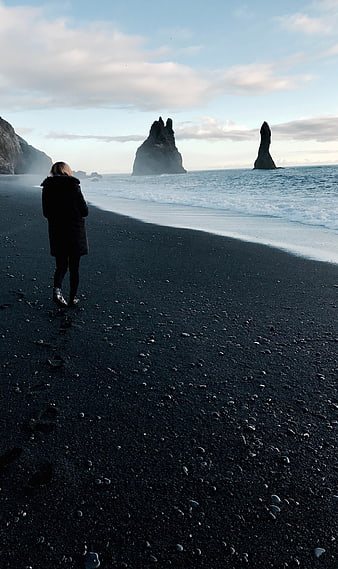 Woman walking on black sand beach with sea stacks