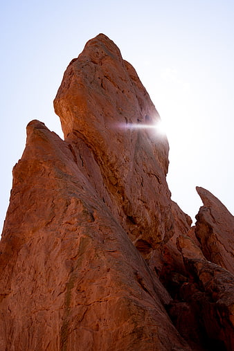 Sun Flare Behind Red Rock Formation in Desert Landscape