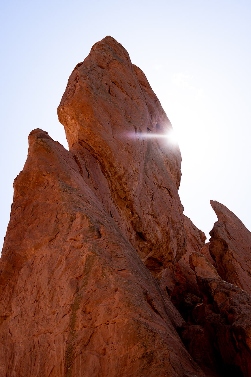 Sun Flare Behind Red Rock Formation in Desert Landscape