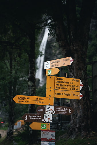 Hiking trail signs with waterfall background in Italian Alps