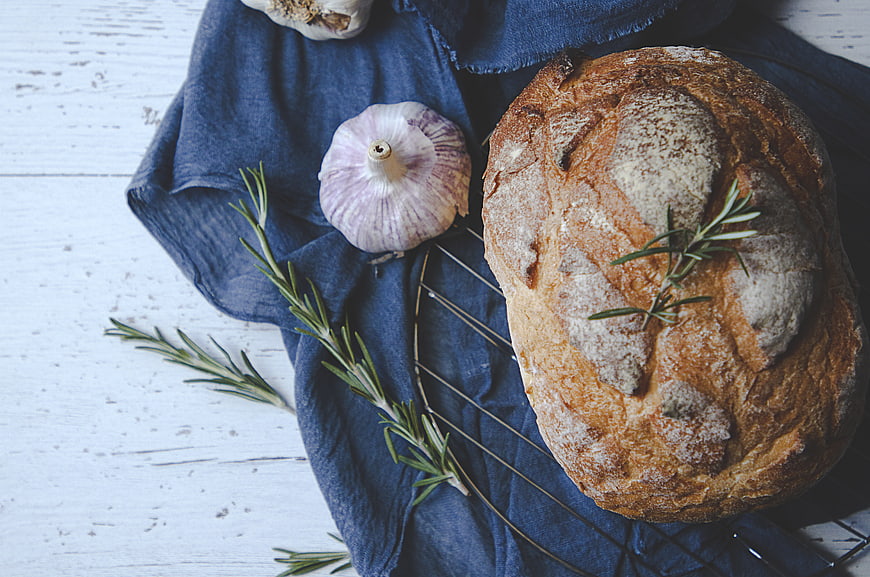 Rustic sourdough loaf with garlic and rosemary on blue linen