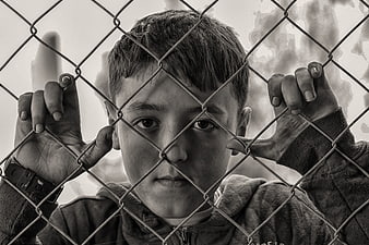 Sad young boy looking through chain link fence