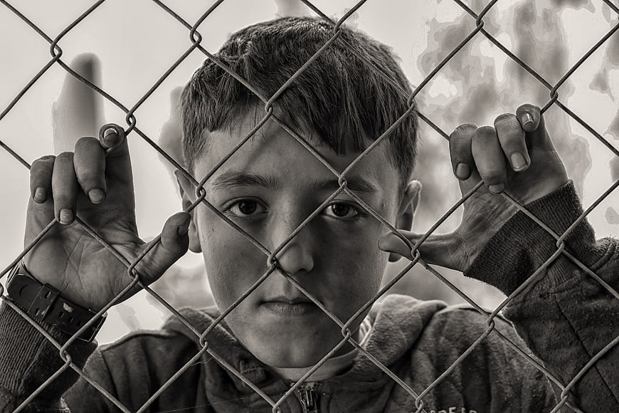Sad young boy looking through chain link fence