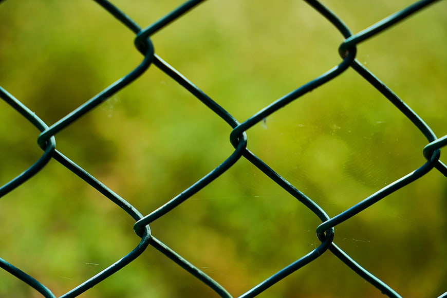 Close-up of chain-link fence with blurred green background