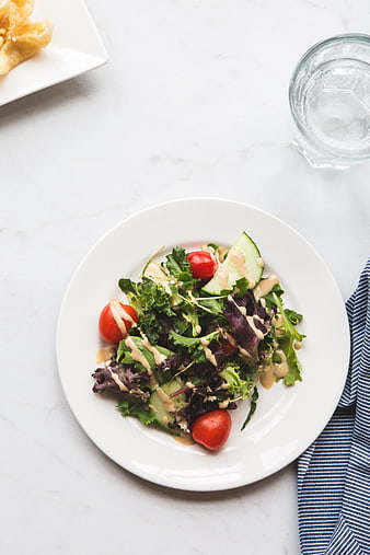 Overhead view of fresh mixed green salad with dressing on white plate