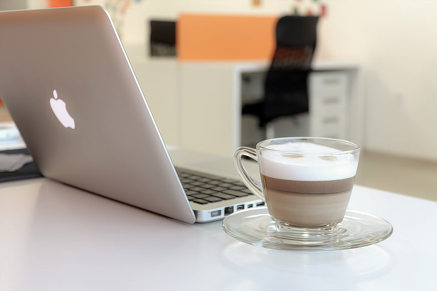 MacBook laptop and layered coffee on white office desk