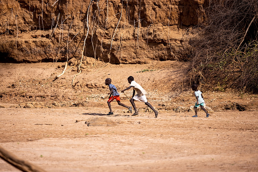 Three African children running and playing in a dry rural landscape