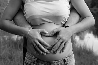 Black and white photo of pregnant belly with hands forming a heart shape