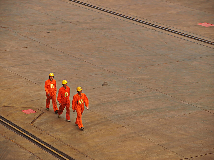 Three industrial workers in orange coveralls walking on tarmac