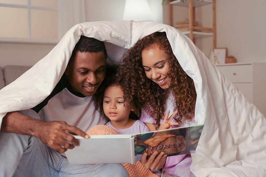 Happy family reading book together under blanket at home