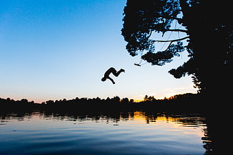 Silhouette of person jumping into lake at sunset