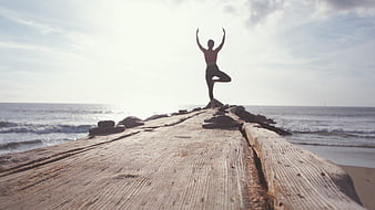 Woman doing yoga on wooden pier at beach
