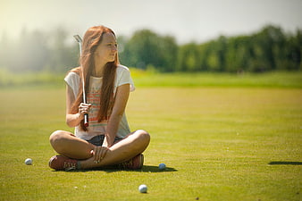 Young woman sitting on golf course holding club