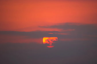 Vibrant orange sunset sun partially obscured by dark clouds