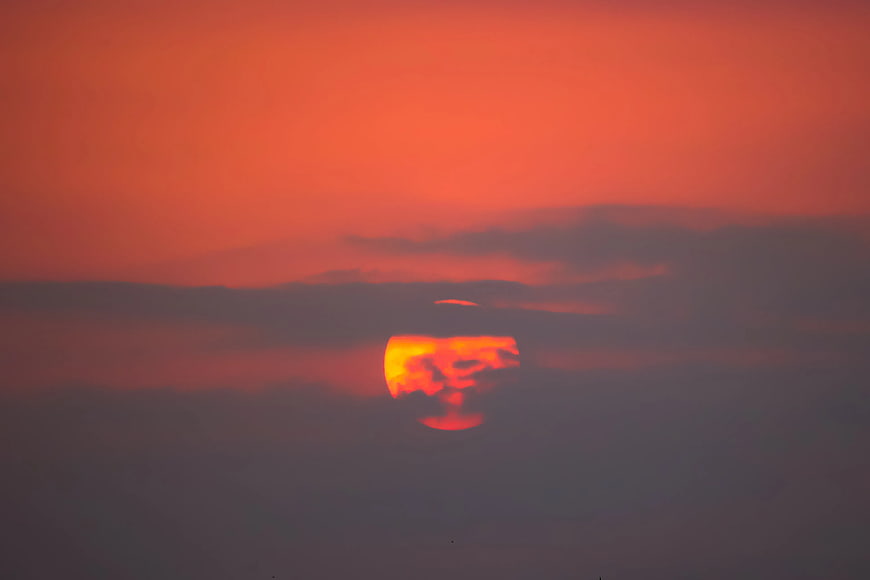 Vibrant orange sunset sun partially obscured by dark clouds
