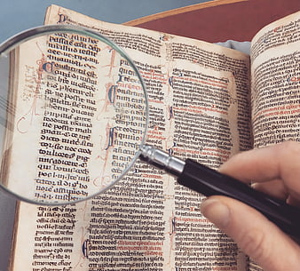 Hand holding magnifying glass over old manuscript text