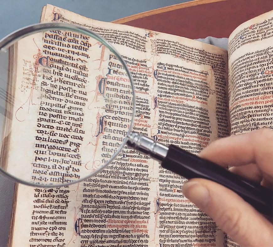 Hand holding magnifying glass over old manuscript text