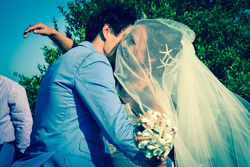 Beach Wedding Couple Kissing Under Veil with Shell Bouquet