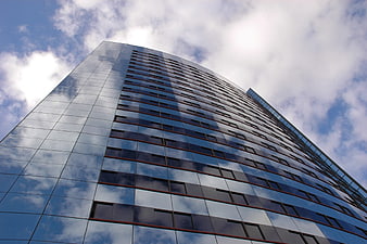 Low angle view of modern glass skyscraper reflecting blue sky