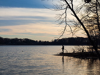 Silhouette of Man Fishing at Dusk on Lake Shore