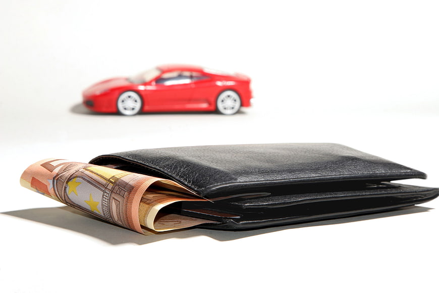 Black wallet with euro banknotes and red toy car on white background