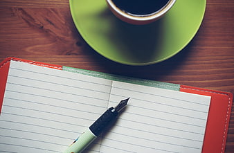 Top view of fountain pen, notebook, and coffee cup on wooden table