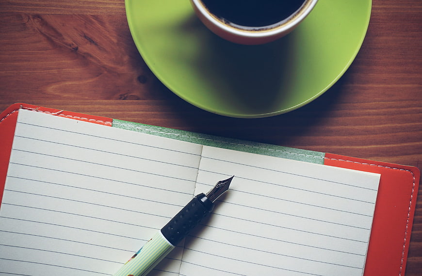 Top view of fountain pen, notebook, and coffee cup on wooden table