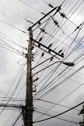 Tangled electrical wires on utility pole against cloudy sky