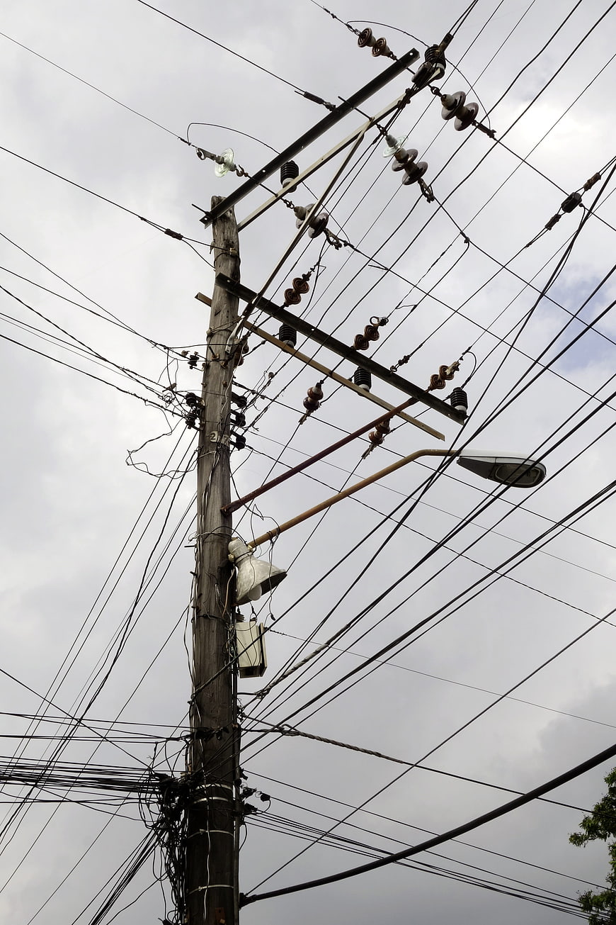 Tangled electrical wires on utility pole against cloudy sky