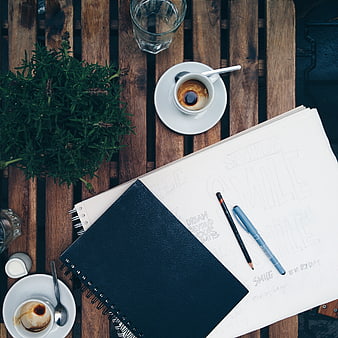 Flat lay of coffee, sketchbook, and pens on wooden table