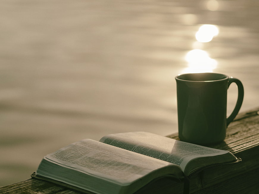 Open Bible and Coffee Mug on Wooden Dock by Lake