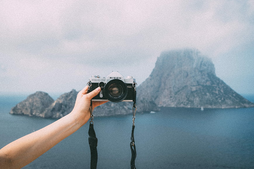 Hand holding vintage Ricoh camera against misty island landscape
