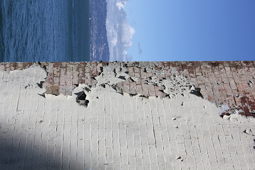 Weathered Brick Wall with Peeling Paint Against Blue Sky and Sea