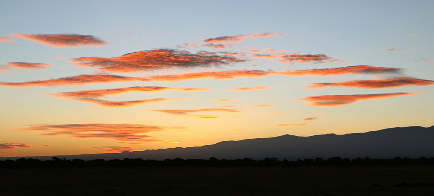 Vibrant orange sunset clouds over dark mountain silhouette