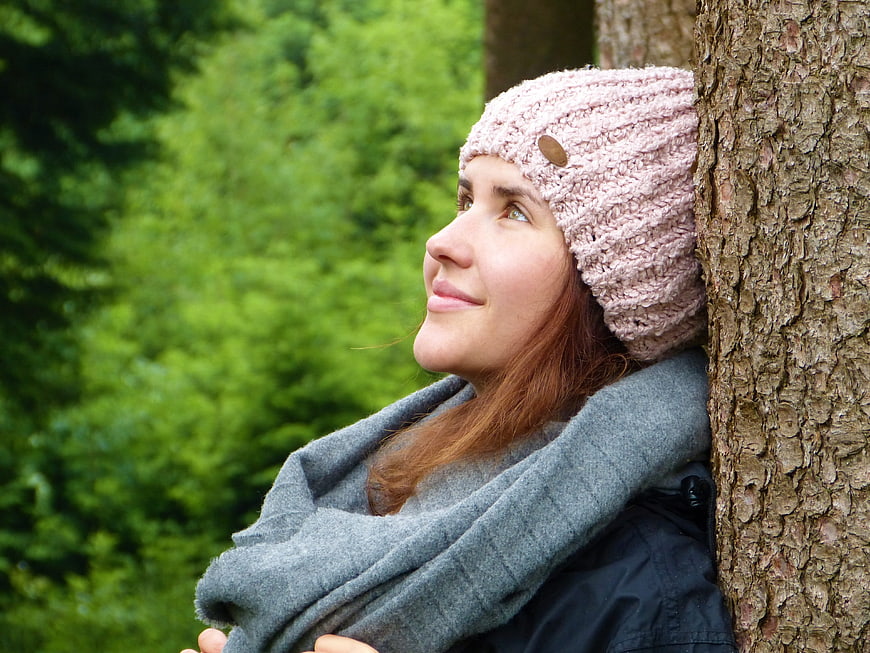 Serene woman in pink hat leaning against tree in forest