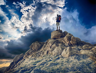 Hiker standing on rocky mountain peak under dramatic cloudy sky