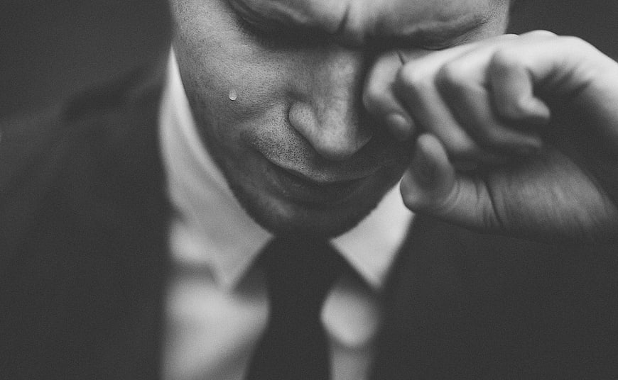 Close-up of crying man in suit wiping tear