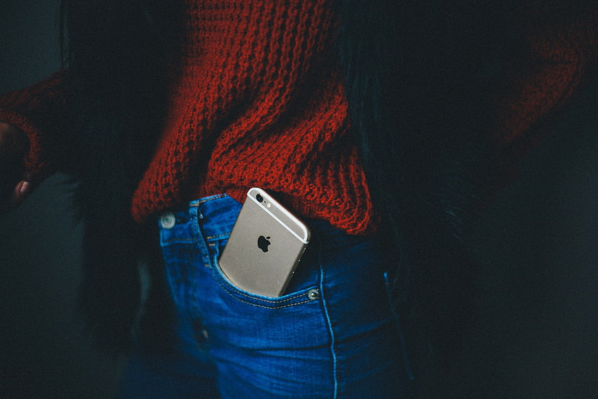 Silver iPhone in blue jeans pocket with red sweater