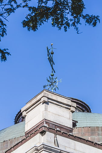 Ornate weathervane on historic building roof against blue sky