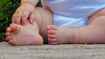 Close-up of baby feet and hand sitting on concrete outdoors