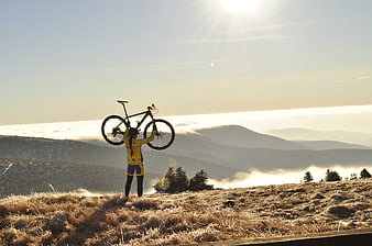 Cyclist holding mountain bike above head on frosty mountain peak