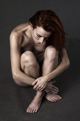 Melancholic Nude Woman Sitting Huddled on Dark Gray Studio Background