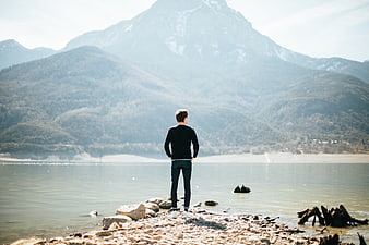 Man standing on rocky shore looking at lake and mountains