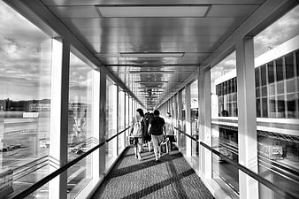 Travelers walking through airport jet bridge in black and white