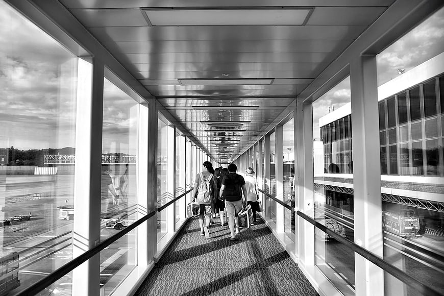 Travelers walking through airport jet bridge in black and white